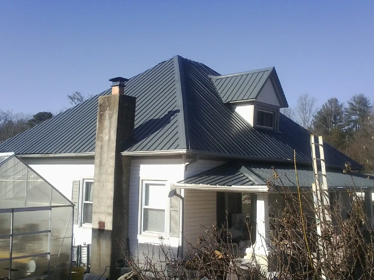Dark blue standing seam metal roof on a white farmhouse with dormer — Slate & Tile Roof Repair by Roofing Brothers in Cayce