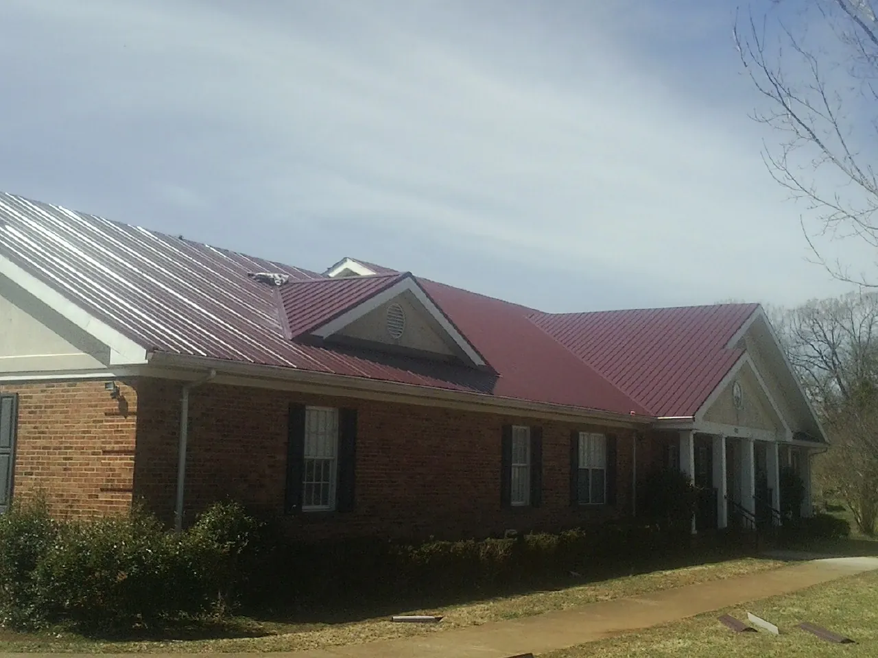 Red metal roof with gabled entries on a long brick building, from a Hail Damage Roof Repair job in Cayce