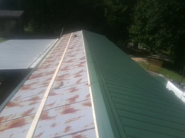 Old rusted panels beside newly installed green metal roofing — Wind Damage Roof Repair by Roofing Brothers in Cayce
